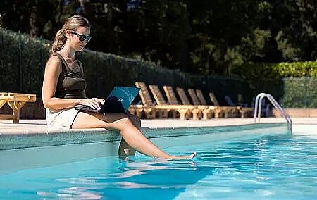 Young woman working on her laptop by the pool, at a Sites et Paysages campsite set in a peaceful natural environment