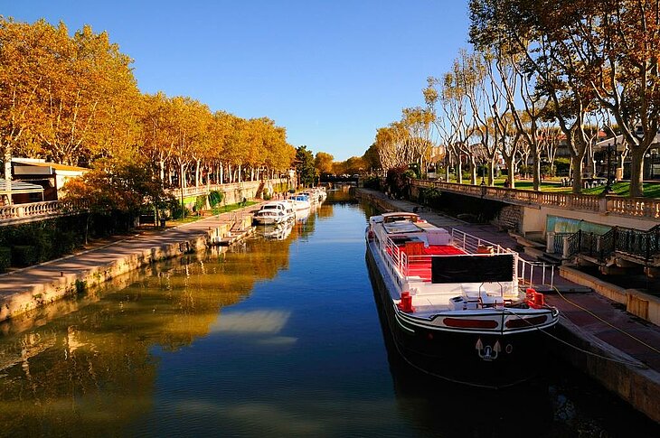 Walk along the Canal de la Robine in Narbonne Barge moored along a canal lined with trees in autumn colours in Narbonne