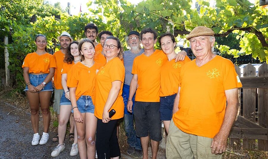 Smiling team at a Sites et Paysages campsite in the Aude, dressed in orange and ready to welcome holidaymakers in a warm, family-friendly atmosphere.