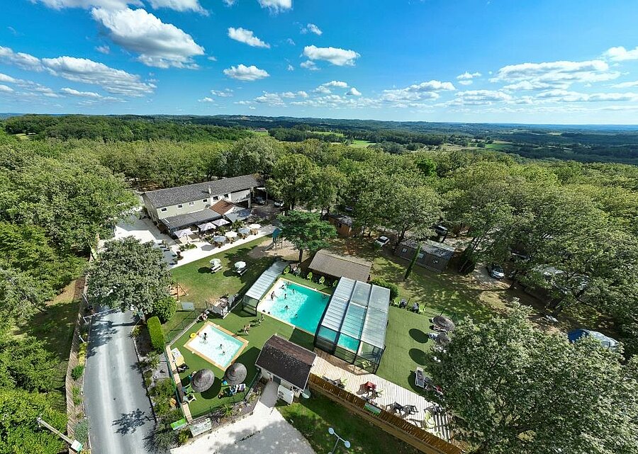Aerial view of a 4-star campsite in the Lot with pools, restaurant, chalets and surrounding forest.