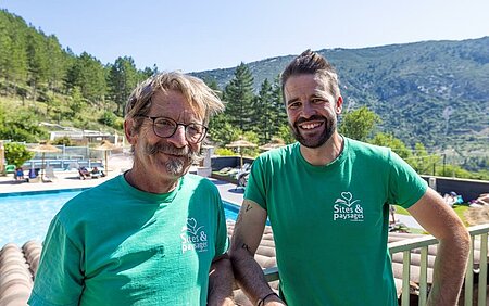 Two smiling owners in front of the pool, at the heart of a nature campsite in the Sites et Paysages network
