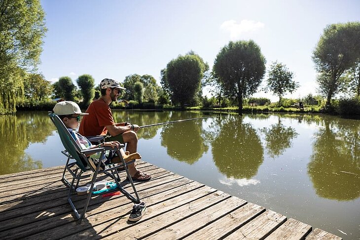 Father and son enjoying a peaceful fishing moment by a lake in Brissac Loire Aubance, surrounded by water and greenery