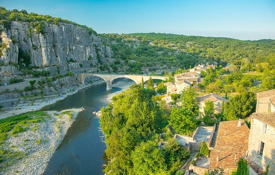 Panoramic view of the Gorges de l'Ardèche with a stone bridge and a typical village, Balazuc, surrounded by nature—ideal for a camping holiday in Auvergne-Rhône-Alpes.