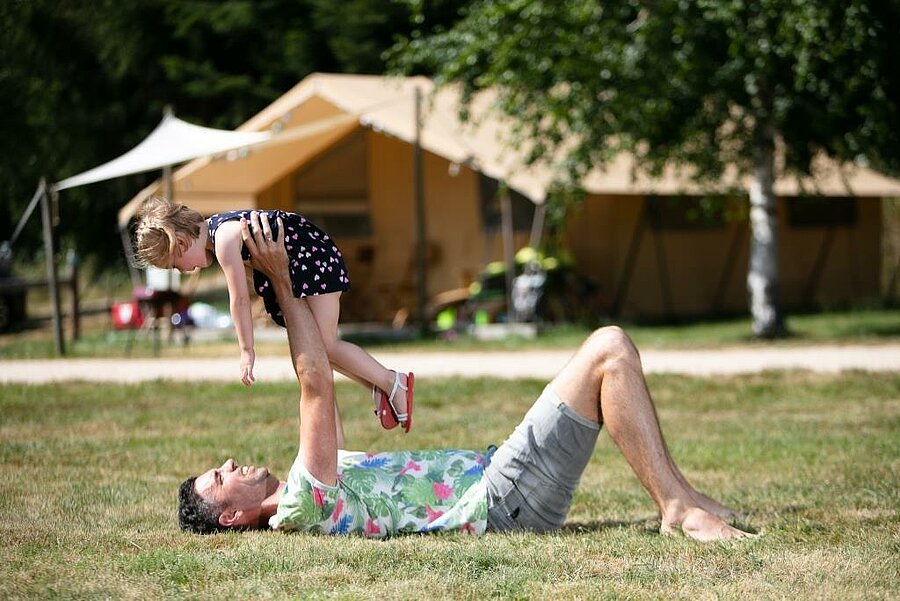 Father playing with his daughter in front of a lodge tent at a family-friendly campsite in Haute-Loire