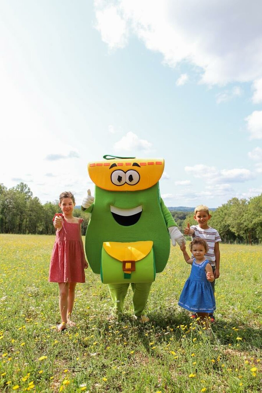 PAKO mascot with children in a flower meadow, last minute August camping in sunny natural surroundings.