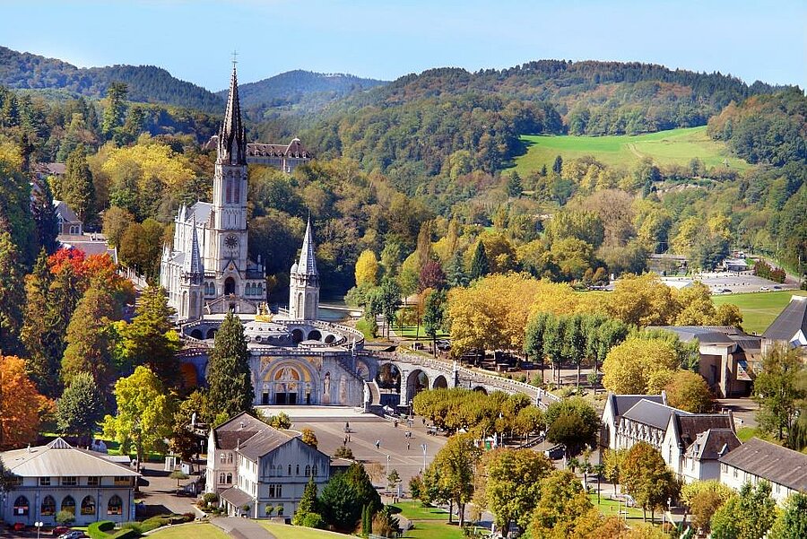 Aerial view of Lourdes sanctuary and basilica nestled in lush forested hills, near a campsite in the Pyrenees.