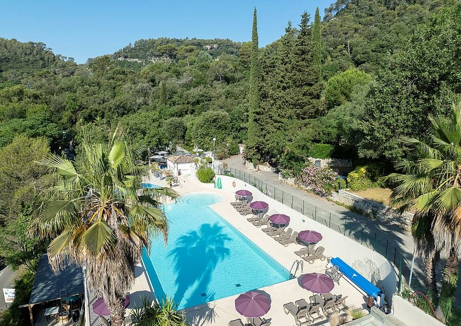 Large swimming pool with sun loungers and umbrellas at 4-star Les Pinèdes campsite, set in greenery near Nice.