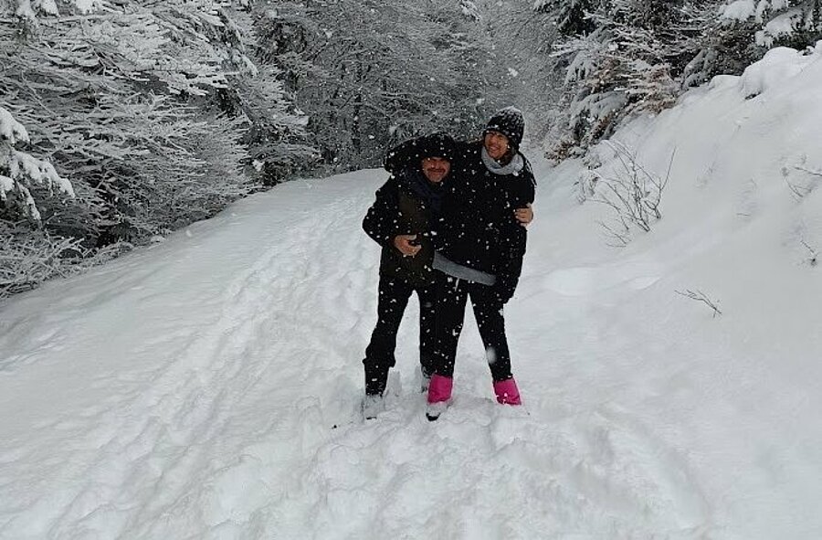 Couple walking on a snowy forest trail with falling snow, winter sports vibe and calm nature—perfect for camping hiver holidays.