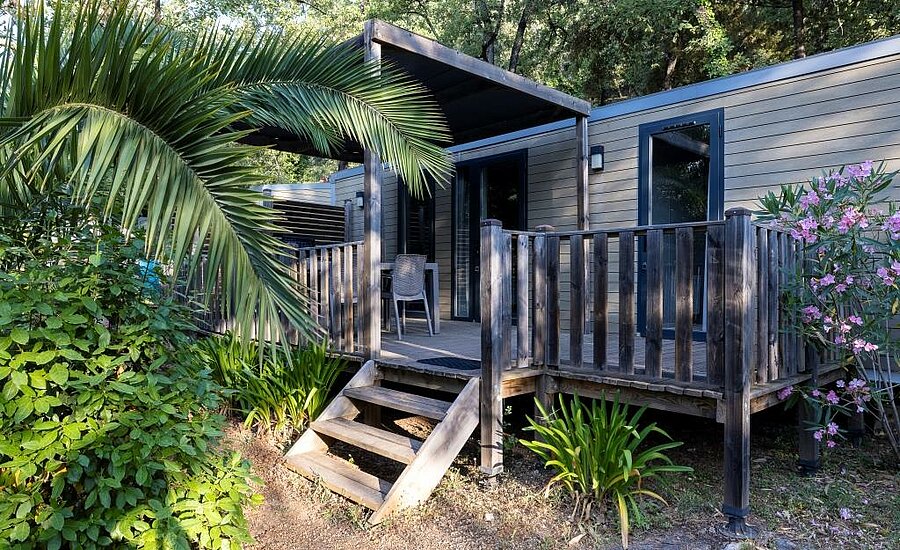 Modern mobile home with wooden terrace and lush greenery, ideal for a mobile home rental in a campsite in France.