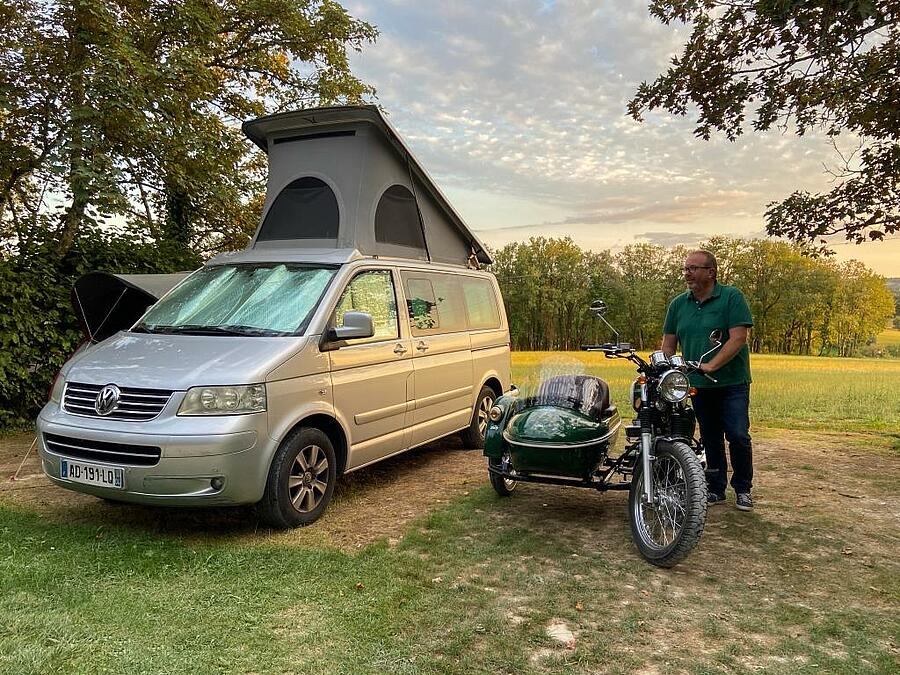 Man with his sidecar next to a van on a spacious pitch.