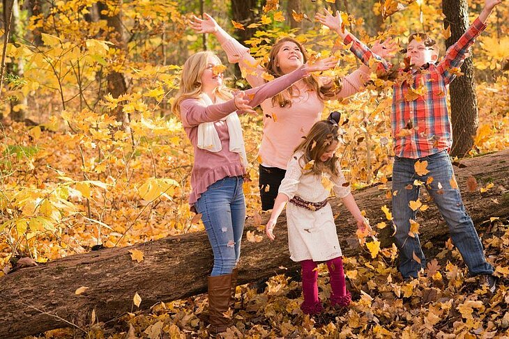 Autumn Games as a Family in the Forest Family playing with fallen leaves in the forest, laughter and autumn colours all around.