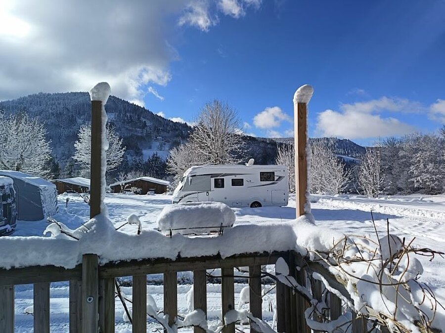 Winter campsite blanketed in snow, with a motorhome parked facing snow-covered mountains. An idyllic setting to enjoy the joys of winter in the heart of nature.