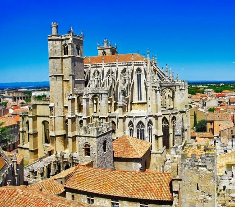 Panorama of Narbonne Cathedral and the ochre rooftops of the city beneath a bright blue sky, a signature of Languedoc-Roussillon.