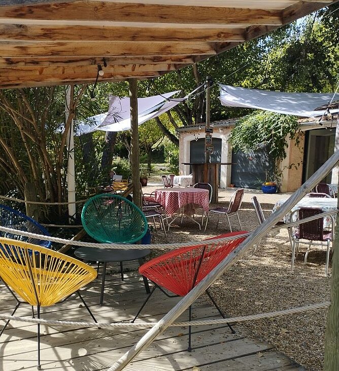 Shaded terrace with tables and colourful armchairs at Domaine de l’Écluse Campsite in Bénivay-Ollon.