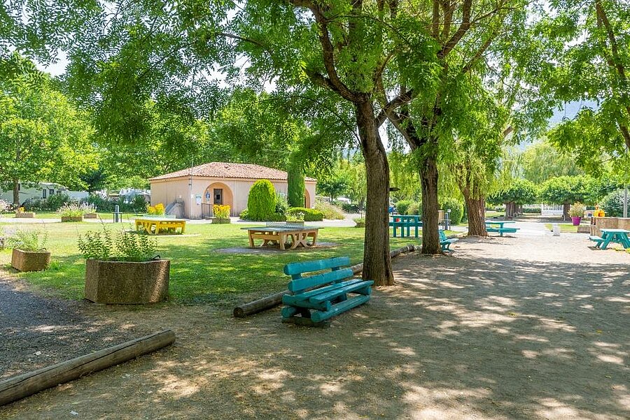 Shaded area with benches and picnic tables at a campsite in the Alpes-de-Haute-Provence, perfect for a family holiday in the heart of nature.