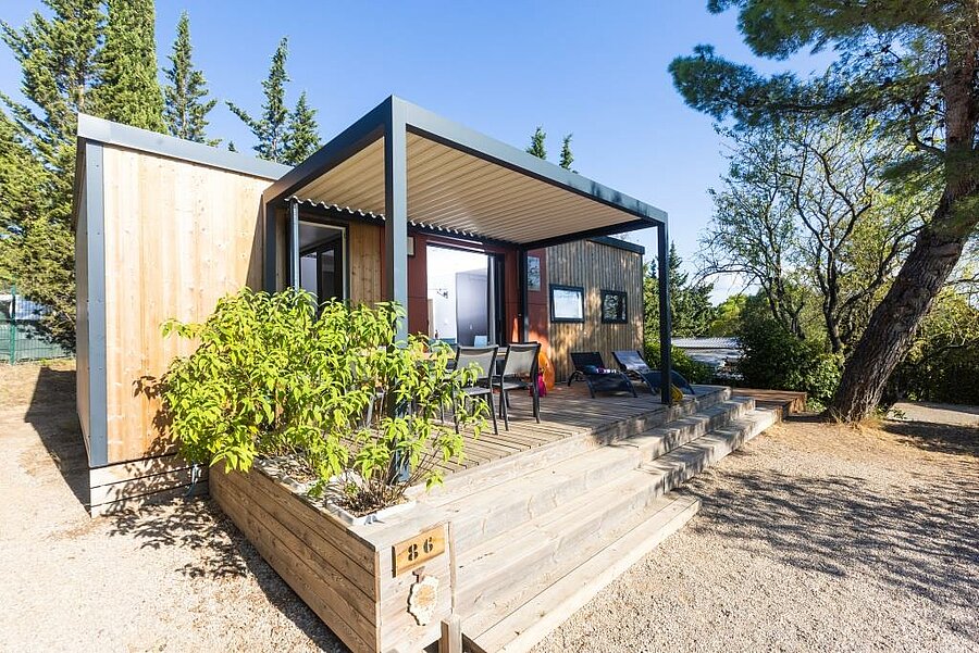 Modern mobile home with wooden terrace and pergola, surrounded by greenery, in a Languedoc-Roussillon campsite. An ideal base for a holiday immersed in nature.