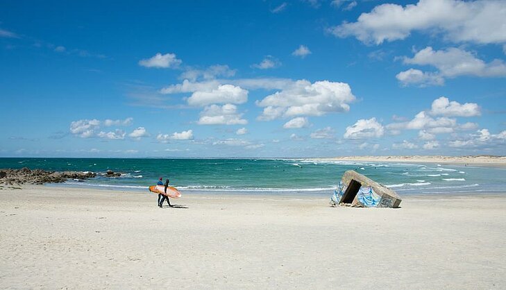 Surf and wild coastline at Pointe de la Torche Surfer walking along the beach at Pointe de la Torche, wild coastline of Finistère, a symbol of nature and freedom in Finistère Tourism.