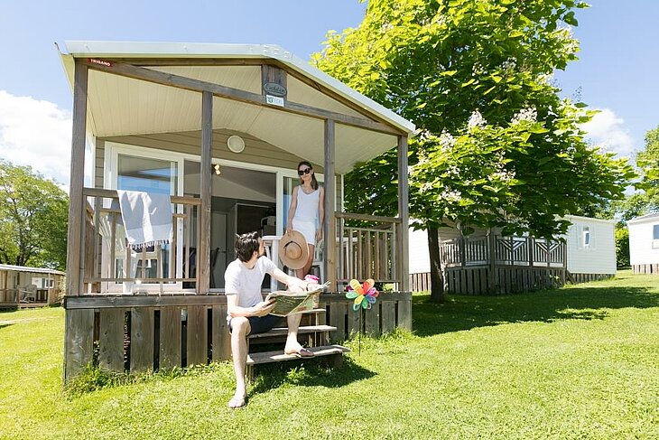 Couple outside a bright mobile home in a human-scale nature campsite, illustrating the early booking couple experience.