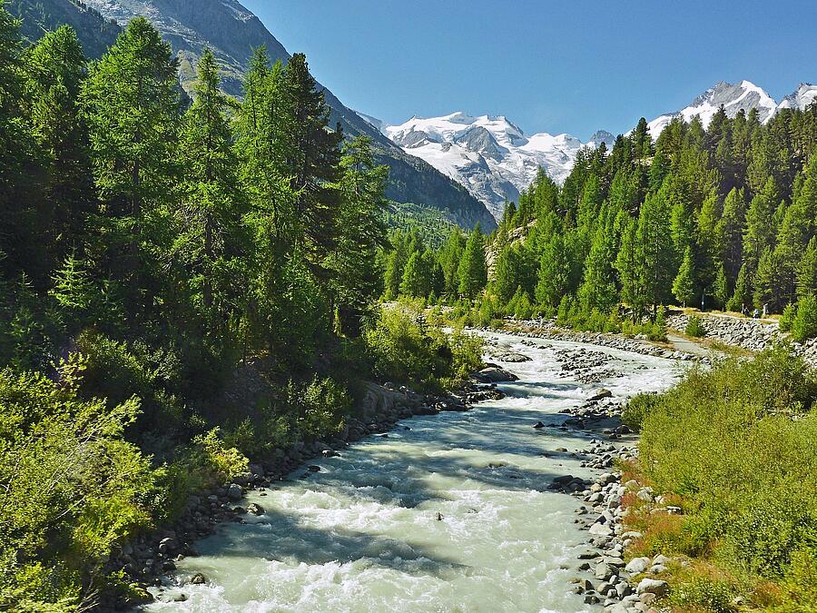 Panoramic view of the Hautes-Alpes featuring a crystal-clear alpine river, lush green forests, and snow-capped peaks. A perfect illustration of the region’s pristine natural beauty, ideal for a camping holiday surrounded by breathtaking landscapes.