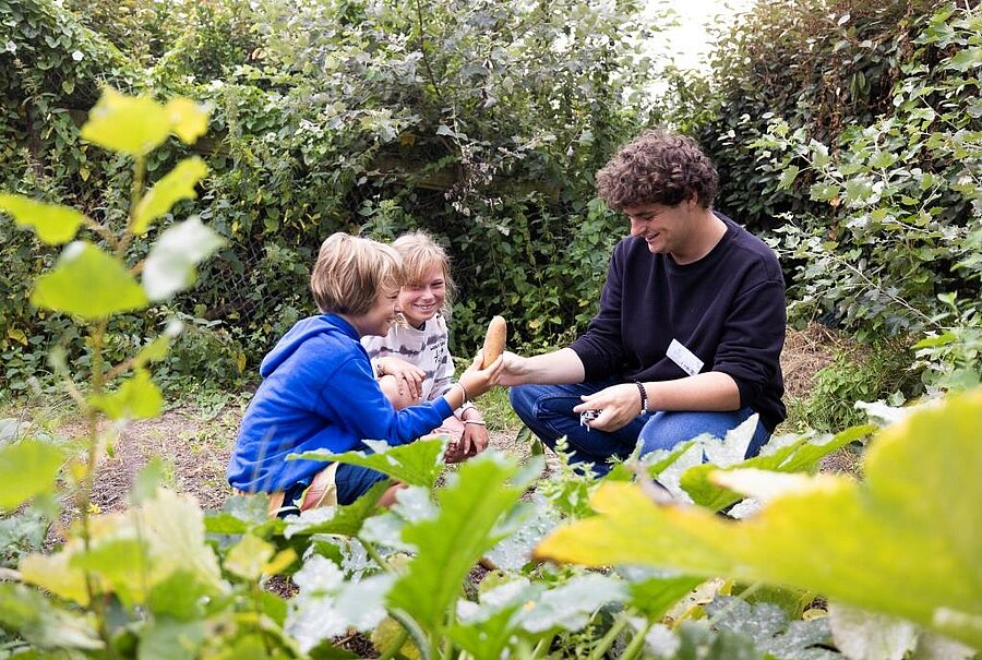 Two children discovering a garden vegetable with a guide in an eco-labeled campsite, reflecting the site's environmental commitment.
