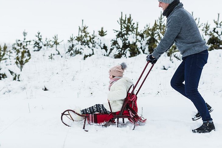 A father and his daughter enjoy the joys of winter sledding in a snowy landscape near La Bourboule. A must-do activity for family fun during a winter break in Auvergne.