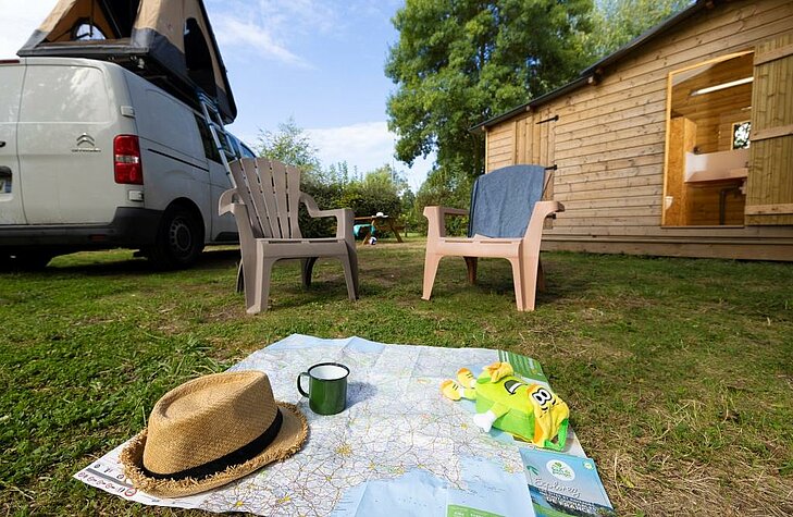 Road map and camper van with rooftop tent in front of a wooden cabin, symbol of a well-prepared Early Booking holiday.