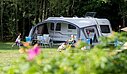 [Translate to Anglais:] Famille installée sur un emplacement de camping pour caravane, en pleine nature, dans un cadre verdoyant et ombragé.