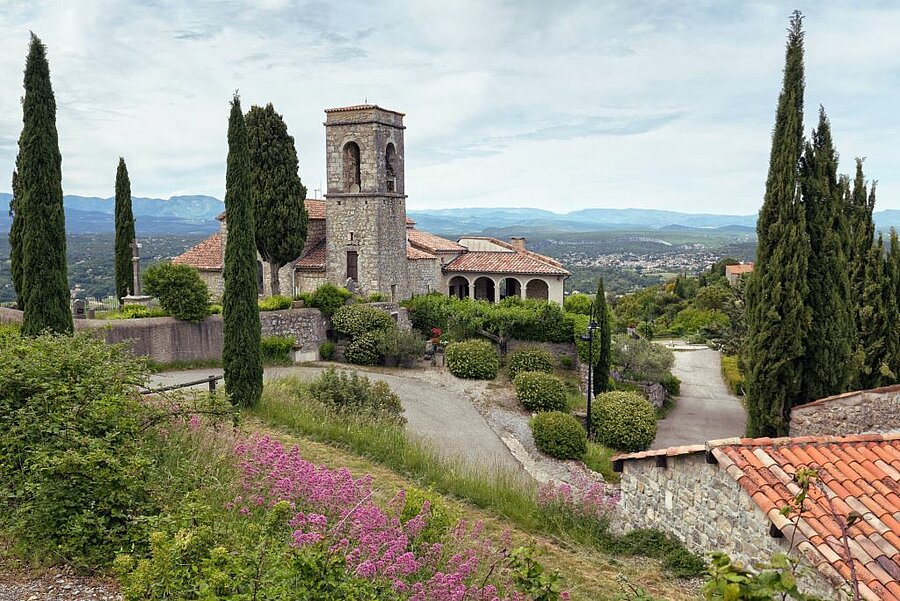 View of Saint-Martin church in Sampzon and the Ardèche valley, surrounded by cypress trees and green hills.