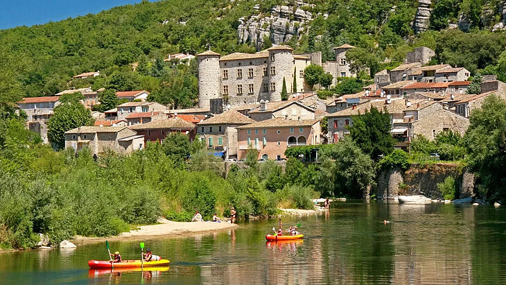 View of Vogüé, its stone houses and castle overlooking the Ardèche, with canoeing and swimming at the foot of the village.