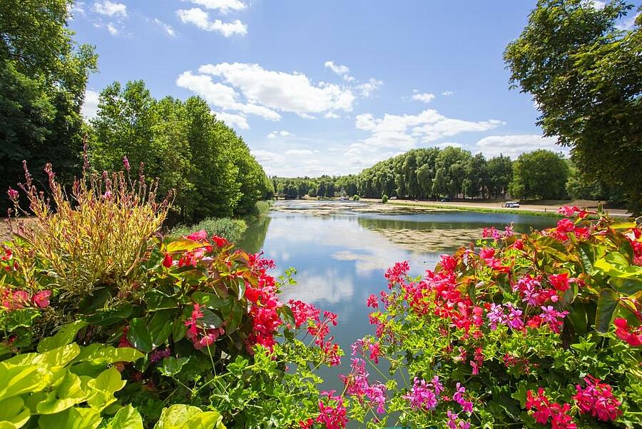 Spring view of a pond surrounded by colorful flowers and lush greenery.