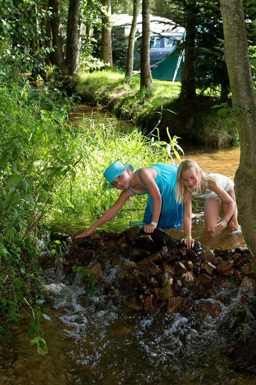 Children playing in a stream near their tent in nature, authentic experience for a family weekend camping.