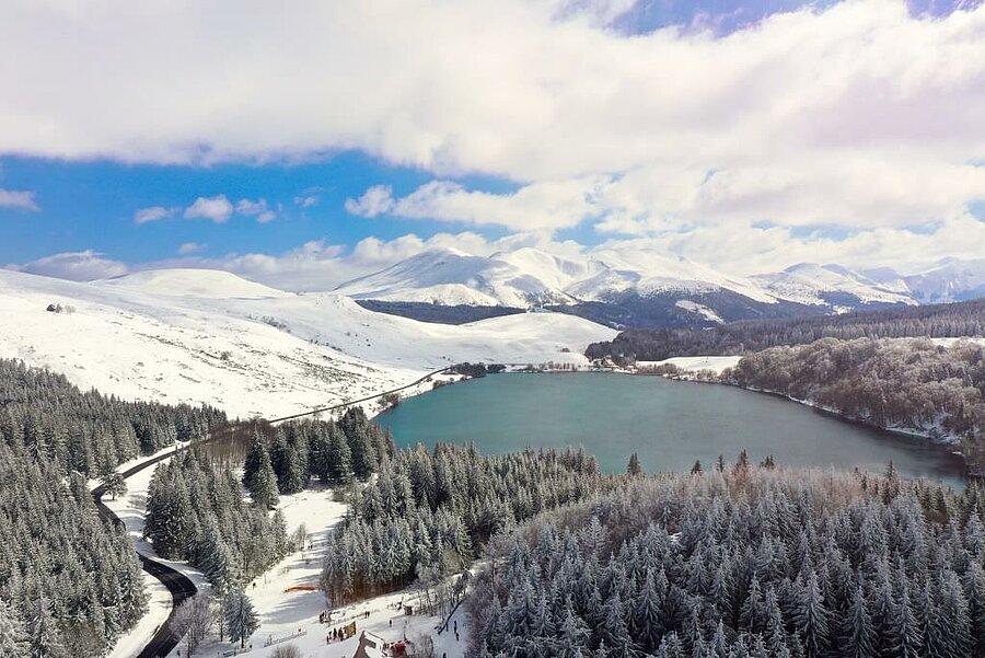 Aerial view of snowy Lake Guery in the Sancy mountains, natural setting for a ski resort campsite close to the peaks.