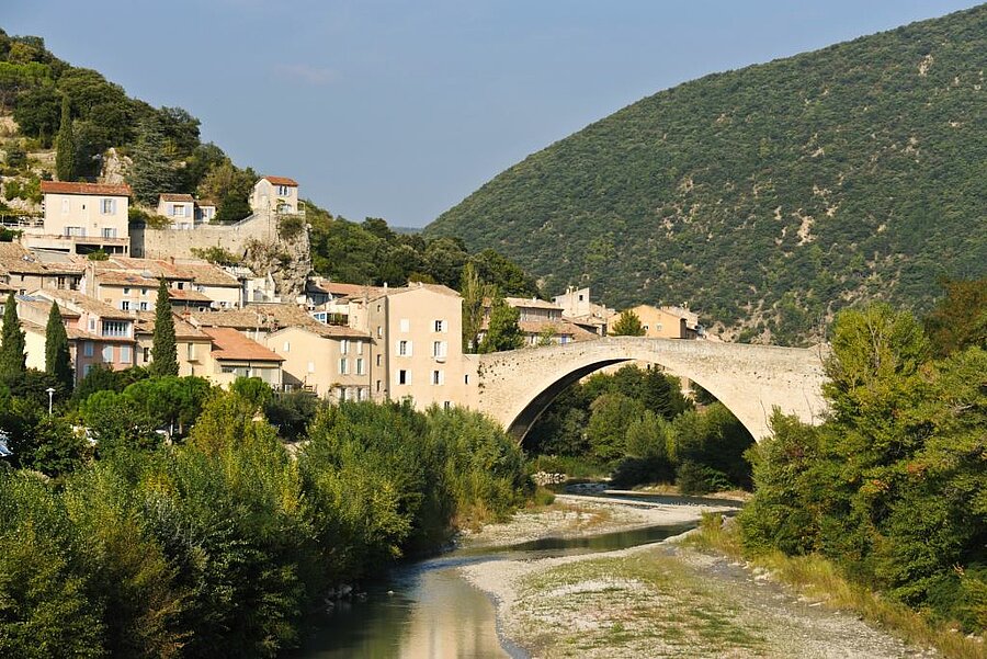 View of Nyons village and its medieval bridge over the river, surrounded by the green hills of Drôme Provençale.