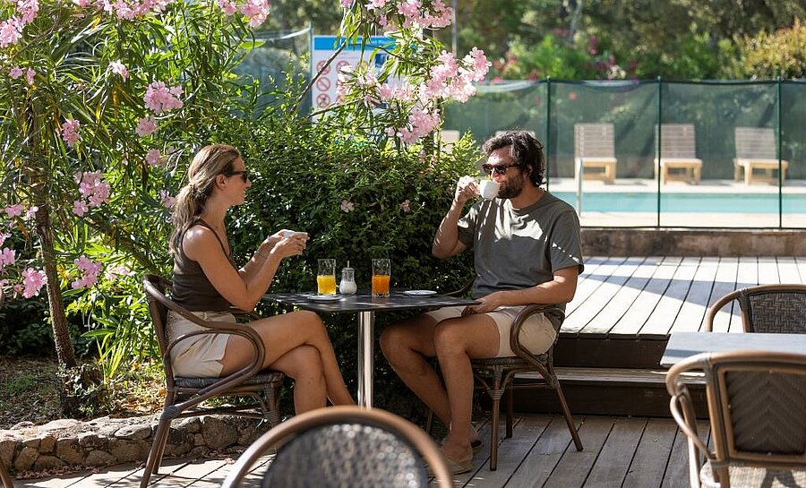 Couple enjoying drinks on a shaded terrace near the pool of a Corsican campsite