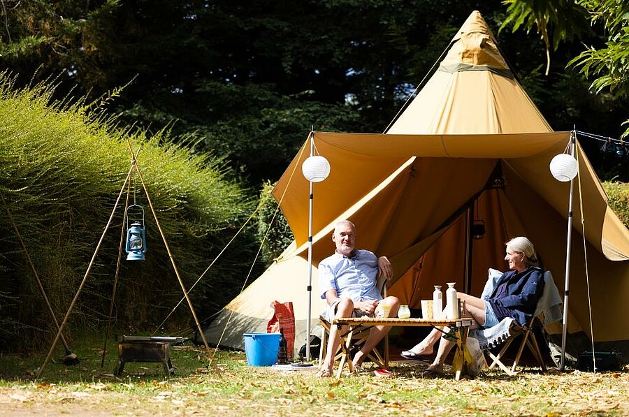 Couple relaxing in front of a unique tent at a campsite in the heart of the Côtes d’Armor – for a nature-filled and comfortable stay in Brittany.