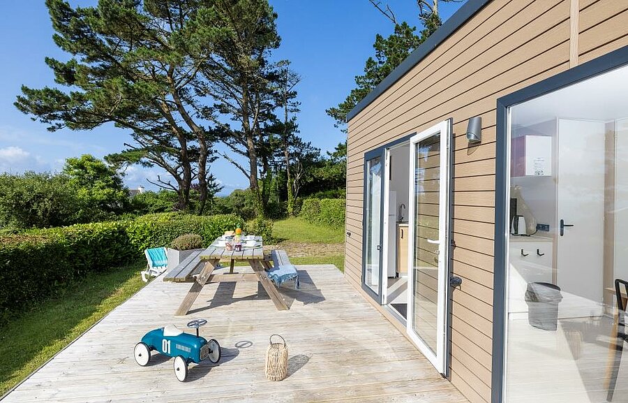 Mobile home rental in Brittany at a campsite, fully equipped mobile home with wooden terrace, outdoor dining area and natural surroundings.