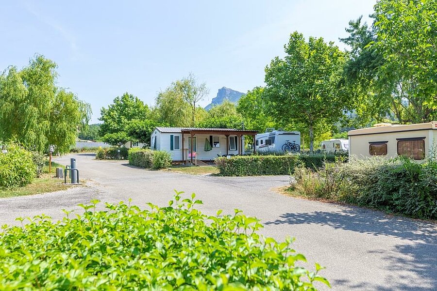 [Translate to Anglais:] Allée et hébergements du camping Les Prés Hauts à Sisteron, avec vue sur les Alpes