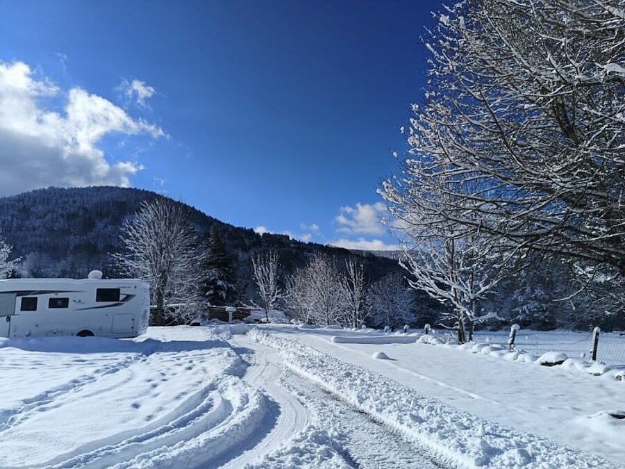 Winter caravanning campsite blanketed in snow, with a motorhome parked in a snowy mountain setting, surrounded by snow-covered trees. An ideal spot for outdoor winter holidays.