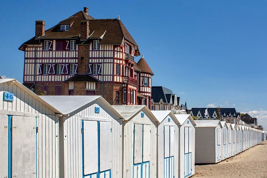 Row of white beach huts in Le Crotoy with a typical seaside villa in the background, an iconic scene of the Baie de Somme.
