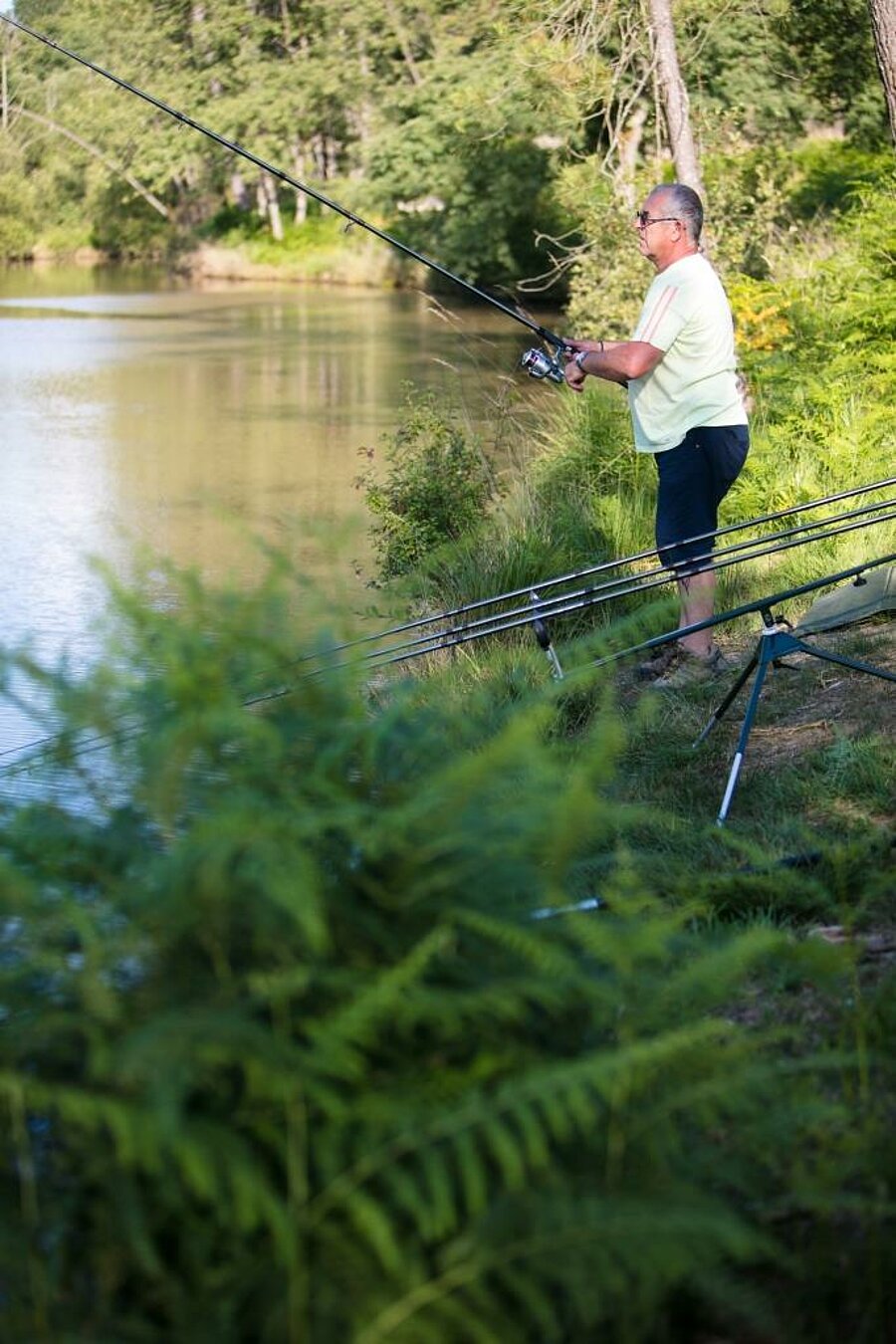 A man fishing on the shore of a lake at a Sites et Paysages campsite—a relaxing nature experience during the Ascension weekend.