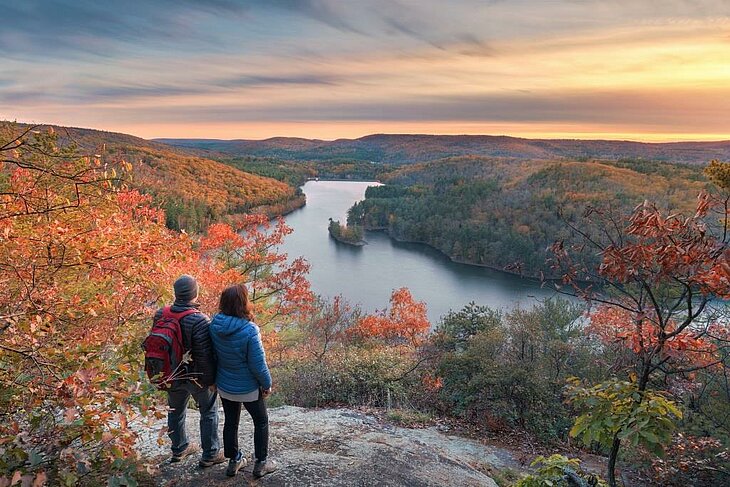 Nature break in September or October Two hikers looking out over a lake surrounded by forests in autumn colours
