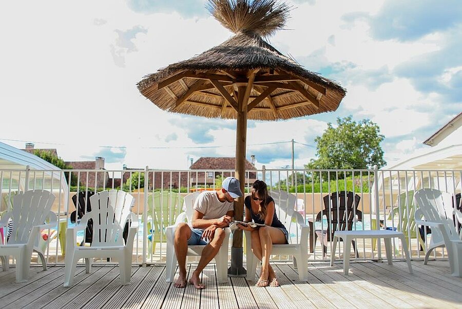 [Translate to Anglais:] Jeune couple en pleine détente sous un parasol en bord de piscine dans un camping pas cher, à la recherche du meilleur rapport qualité-prix.