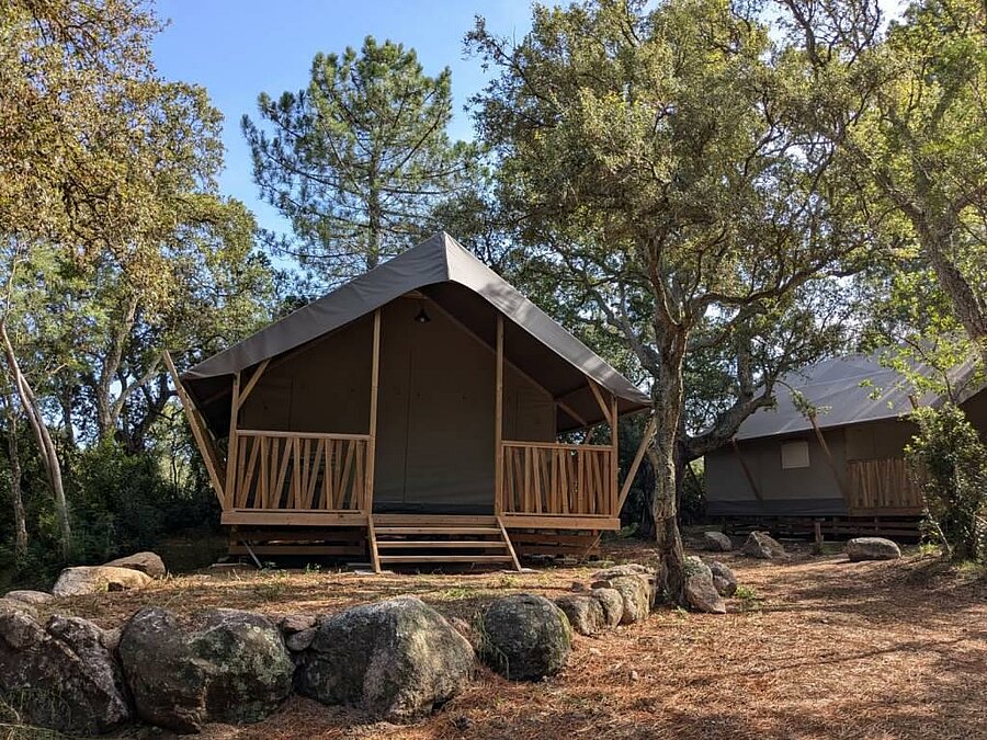 Wooden glamping tent nestled among trees in an eco-labeled campsite in Corsica, offering sustainable accommodation in harmony with the environment.
