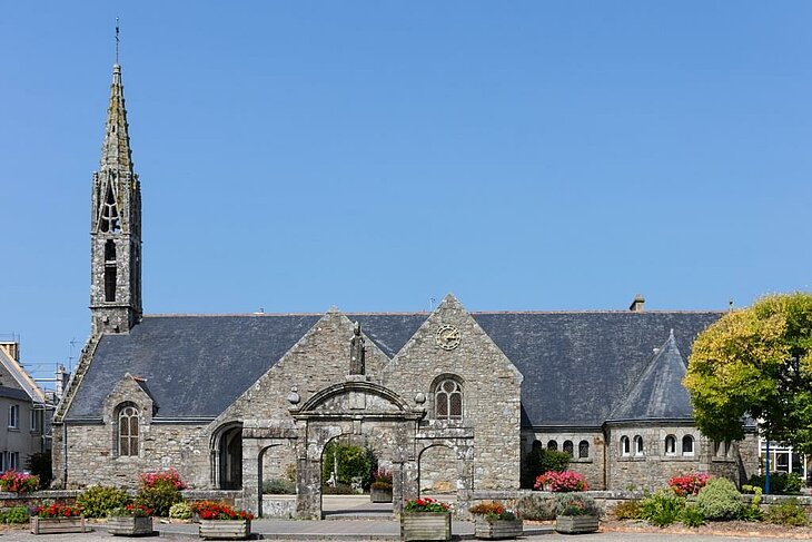 Granite façade of Saint-Magloire Church in Telgruc-sur-Mer, surrounded by flowers and a symbol of local heritage.