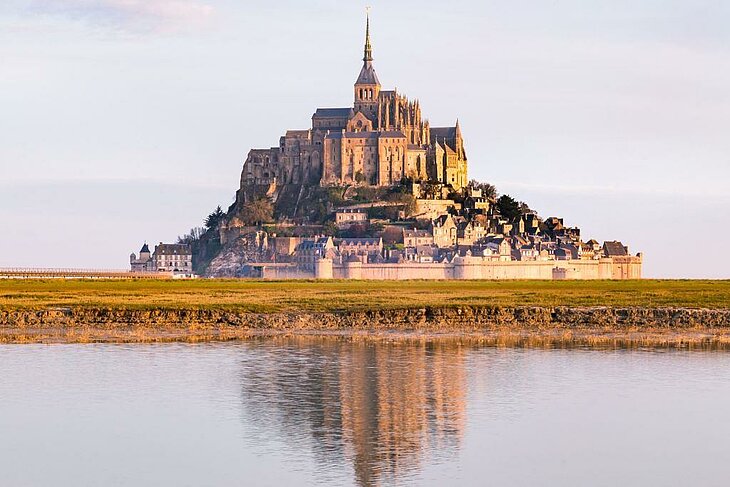 View of Mont-Saint-Michel in Normandy at sunset, with its majestic abbey and reflections over the salt meadows, a must-see visit for retirees.