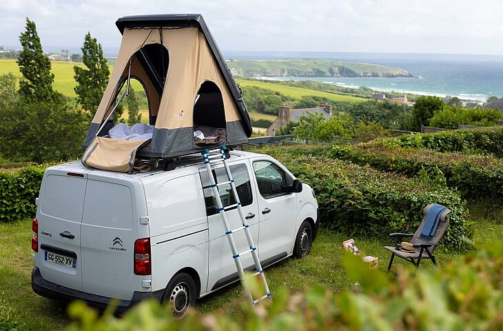Camper van with rooftop tent on a green pitch overlooking the sea, perfect for a comfortable nature stay.
