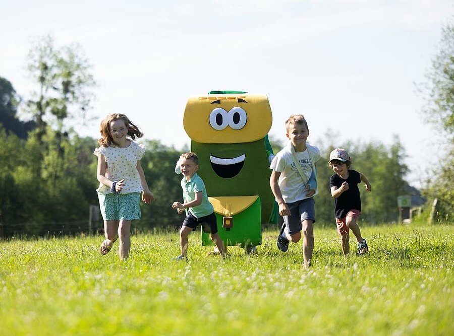 Children running on grass with a mascot at a campsite, friendly family holidays atmosphere in nature.