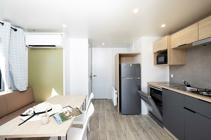 Living area and kitchen of a mobile home equipped with a wall-mounted air conditioning unit.