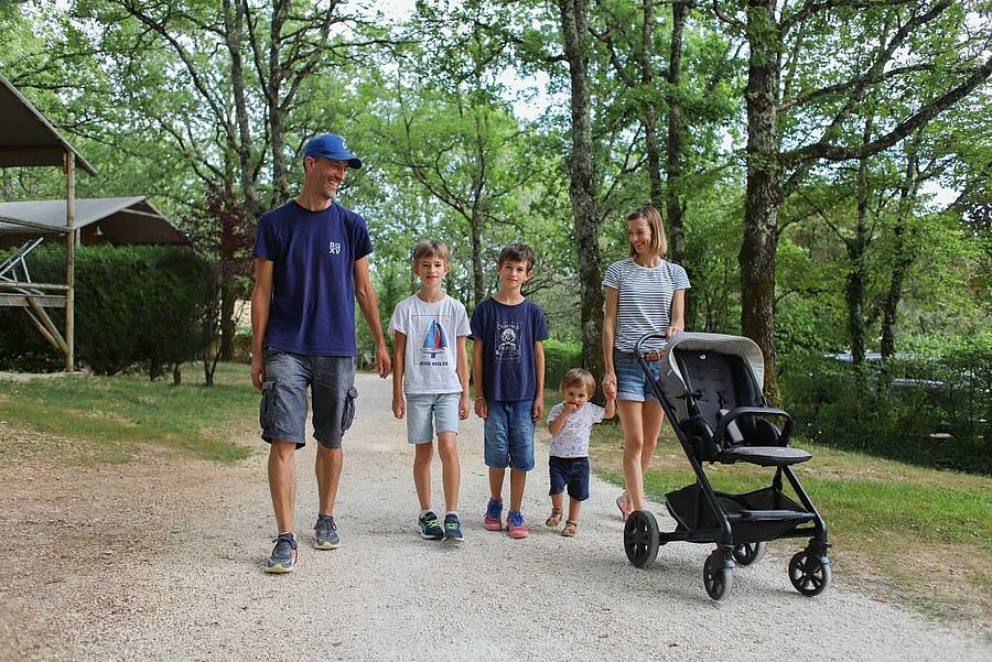 Family with children and stroller walking through a leafy campsite, peaceful setting for a family weekend.