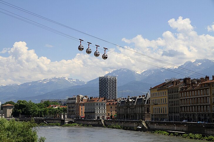 View of the Grenoble cable car with snow-capped mountains in the background, a symbol of Auvergne-Rhône-Alpes and Isère, where city meets nature